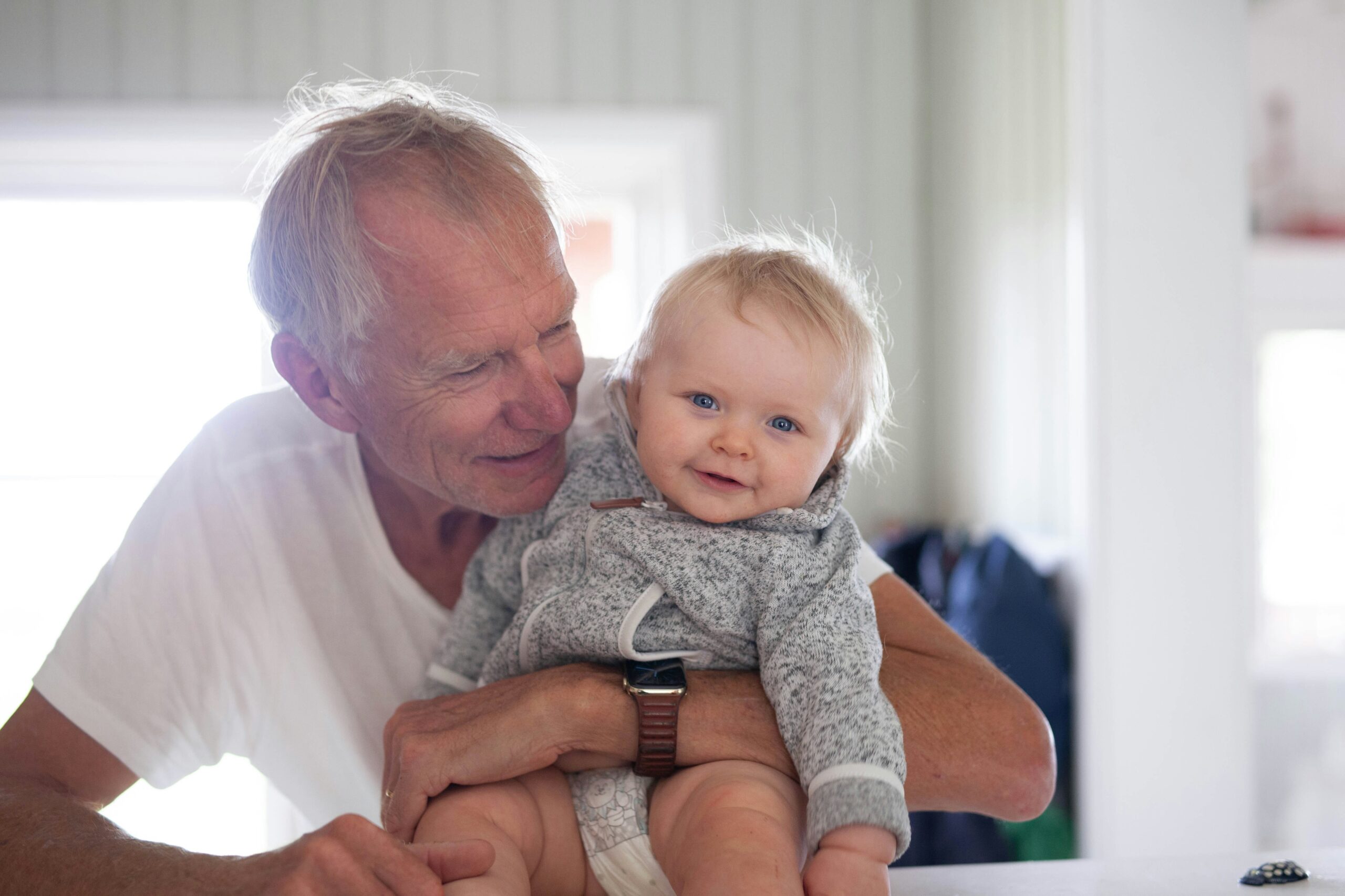 Senior man lovingly holding baby in cozy home setting, illustrating financial security for future generations