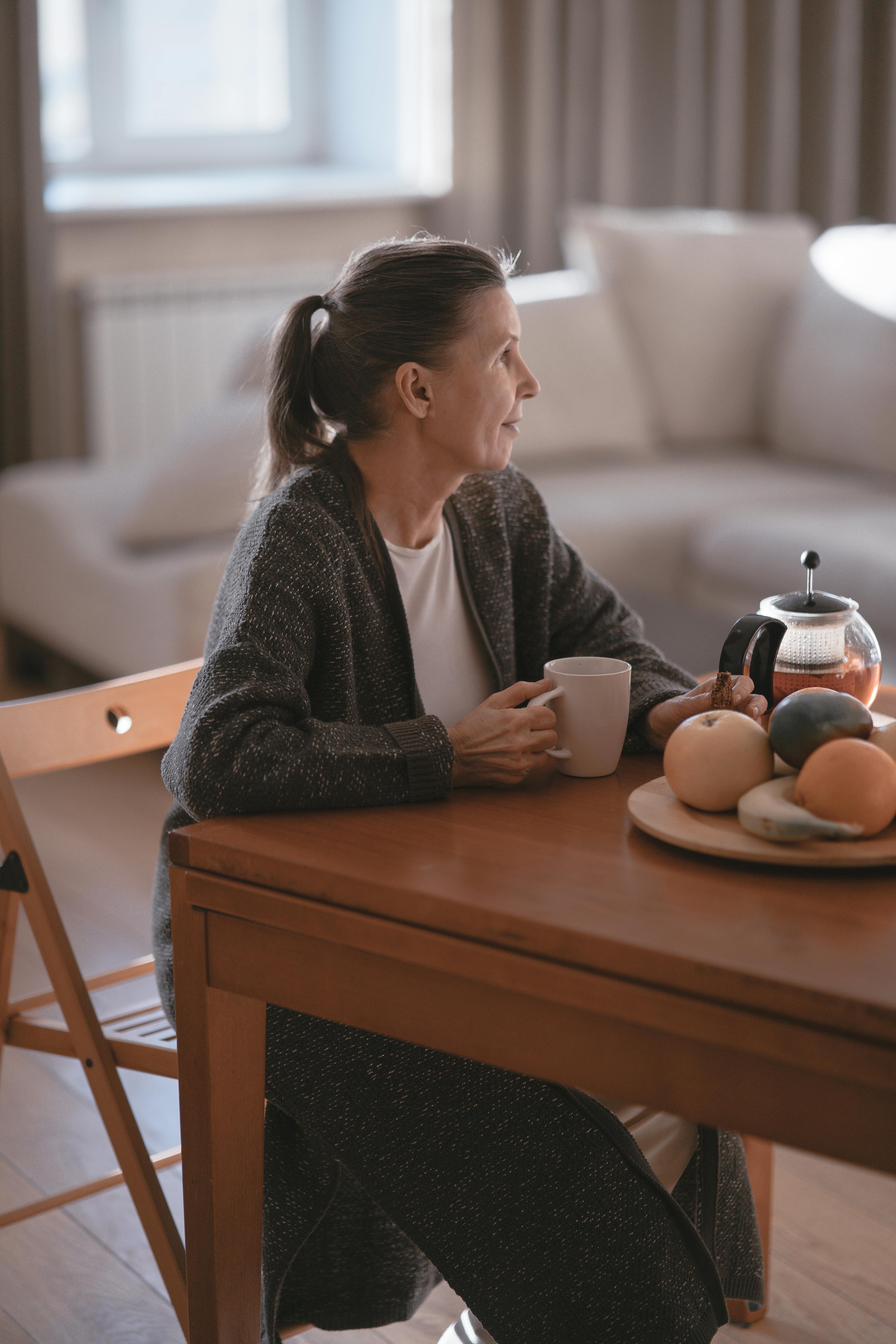 Senior woman sitting at home with coffee, thoughtfully considering Medicare plan options.