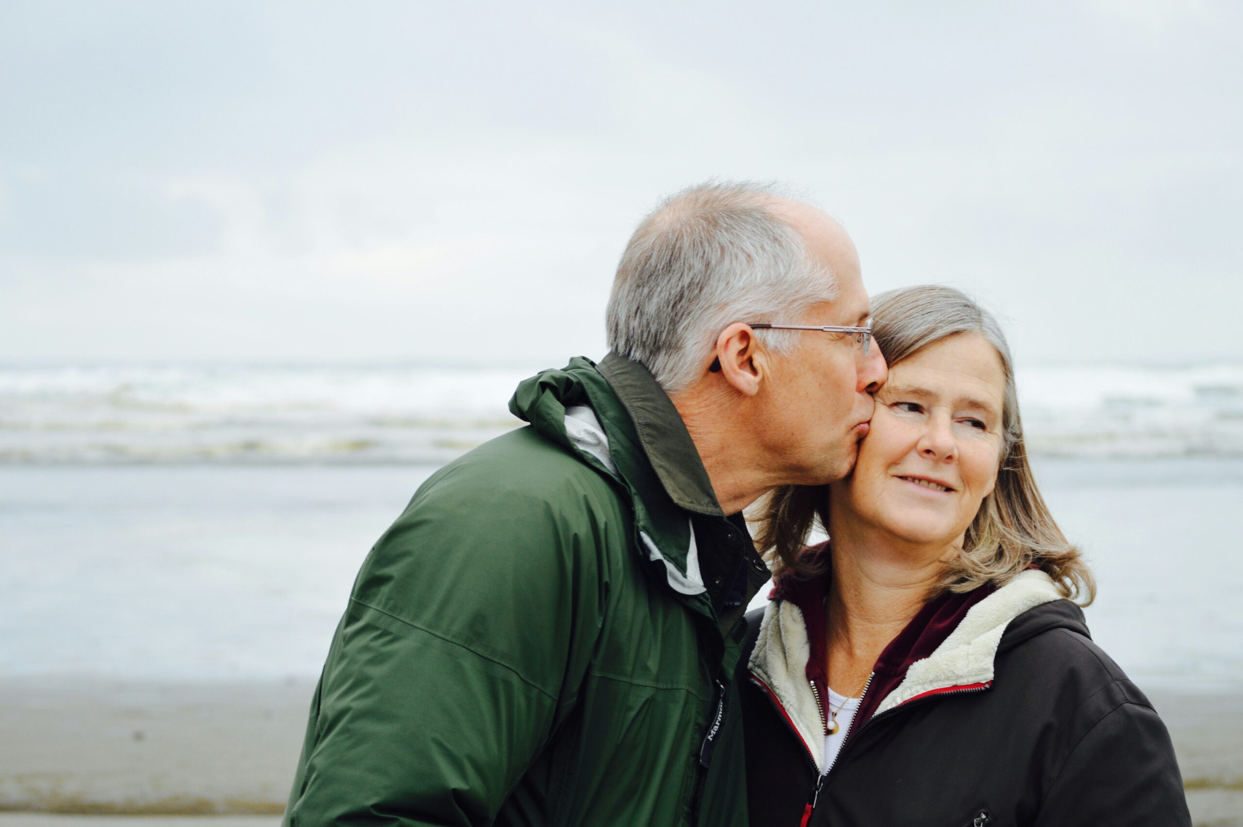 Senior man kissing woman on beach, representing peace of mind through retirement and life insurance planning